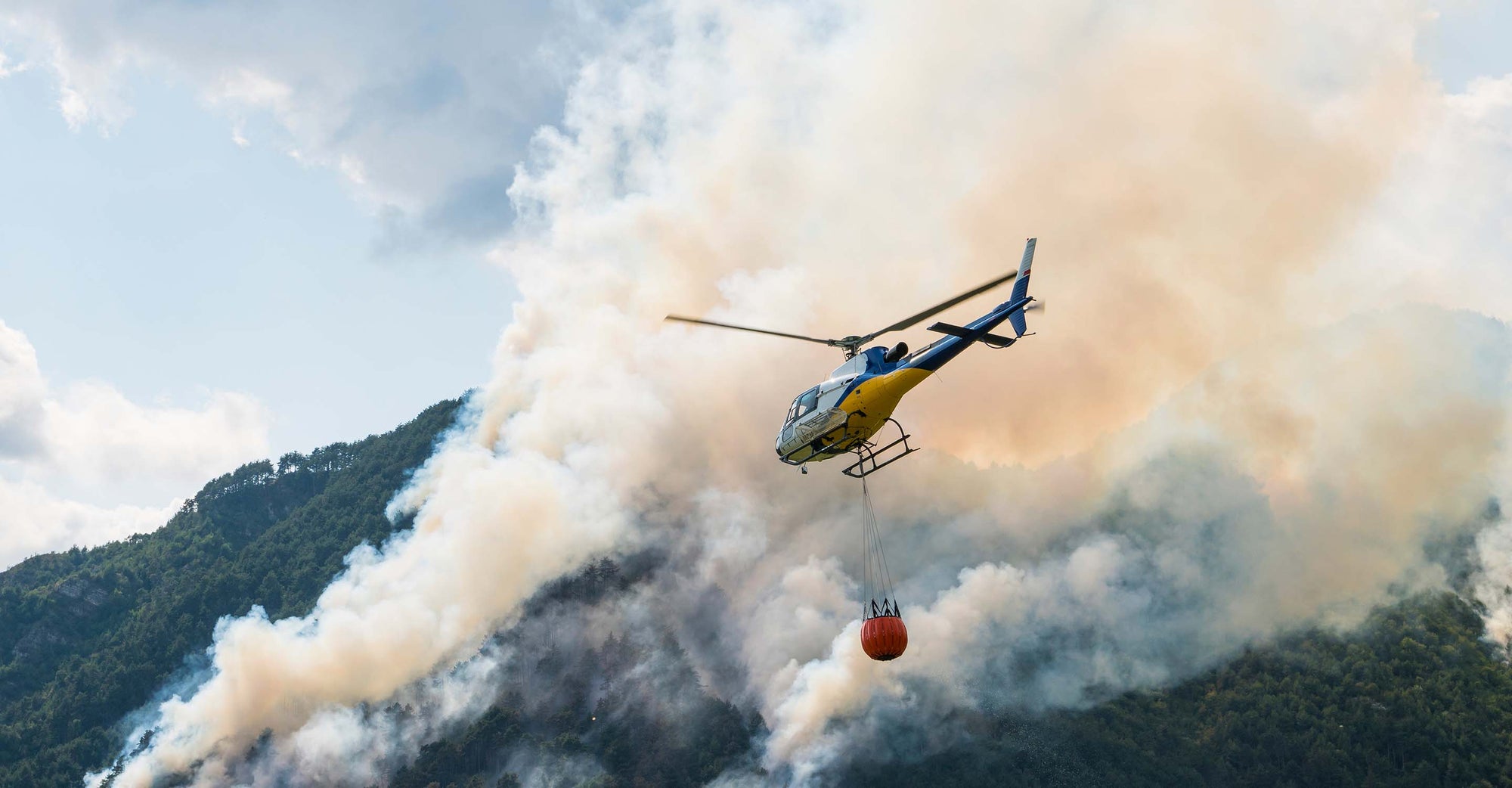 Firefighting helicopter flying above wildfire with water tank