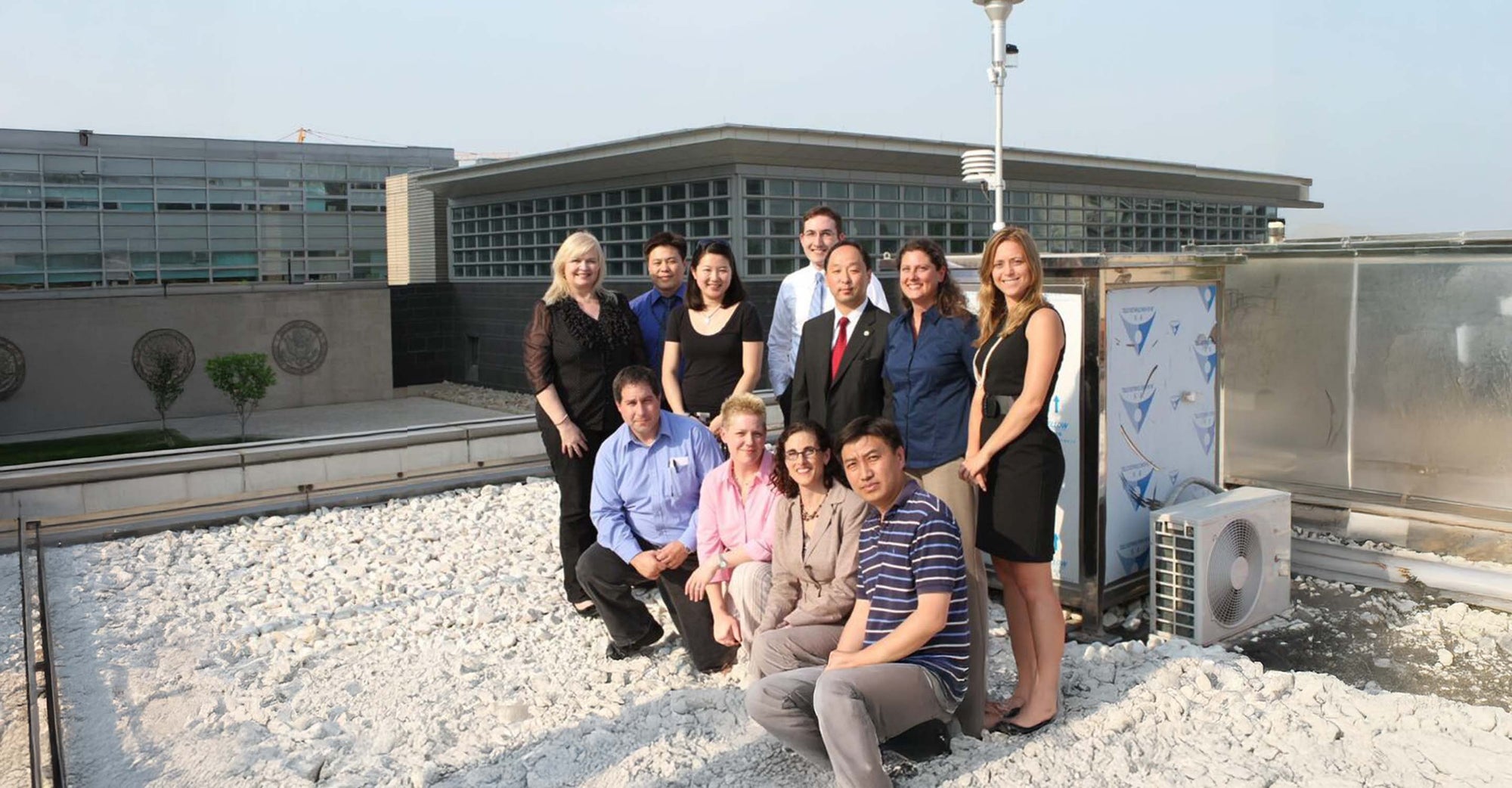Group of people on rooftop standing in front of an air quality monitor.